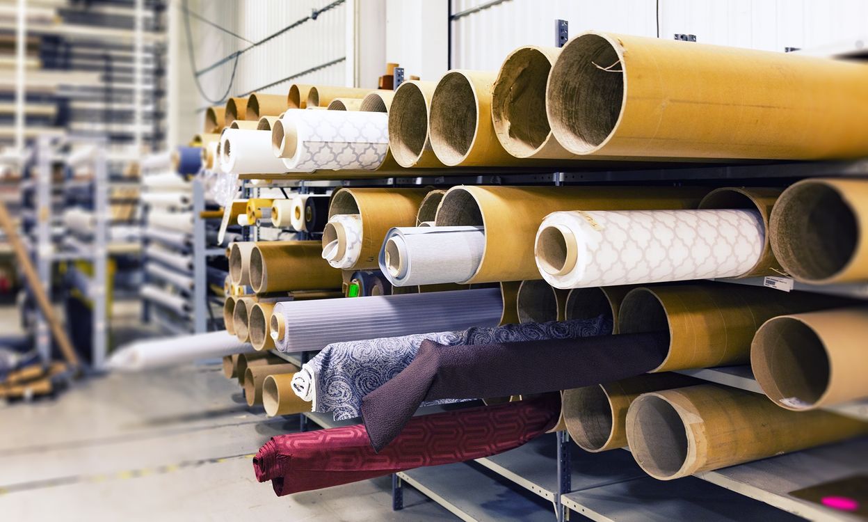Rows of stacked fabric rolls in a textile warehouse showing the raw material stage of clothing cost breakdown