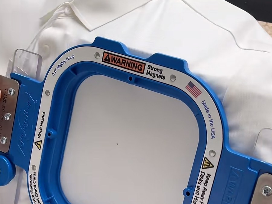 White polo shirt clamped in a magnetic embroidery hoop at a corporate uniform manufacturer