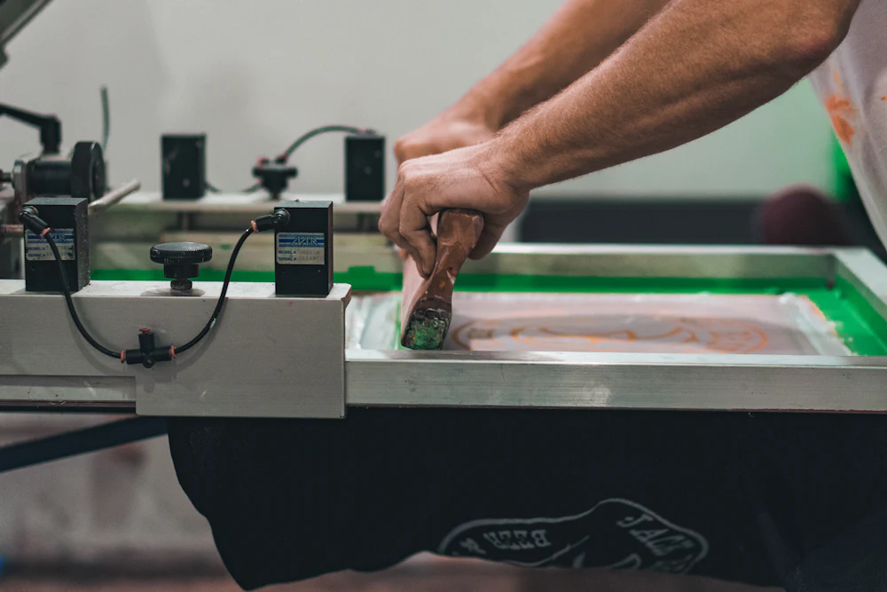 Worker pulling ink across a screen printing frame onto a black garment