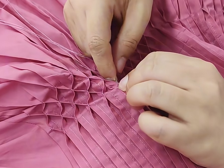 Machinist hand-finishing smocking on a pink dress for a fashion brand clothing manufacturer order