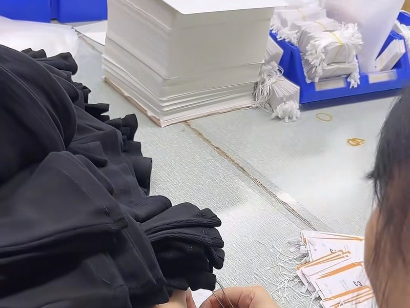 Worker attaching size hangtags to folded black garments before packaging
