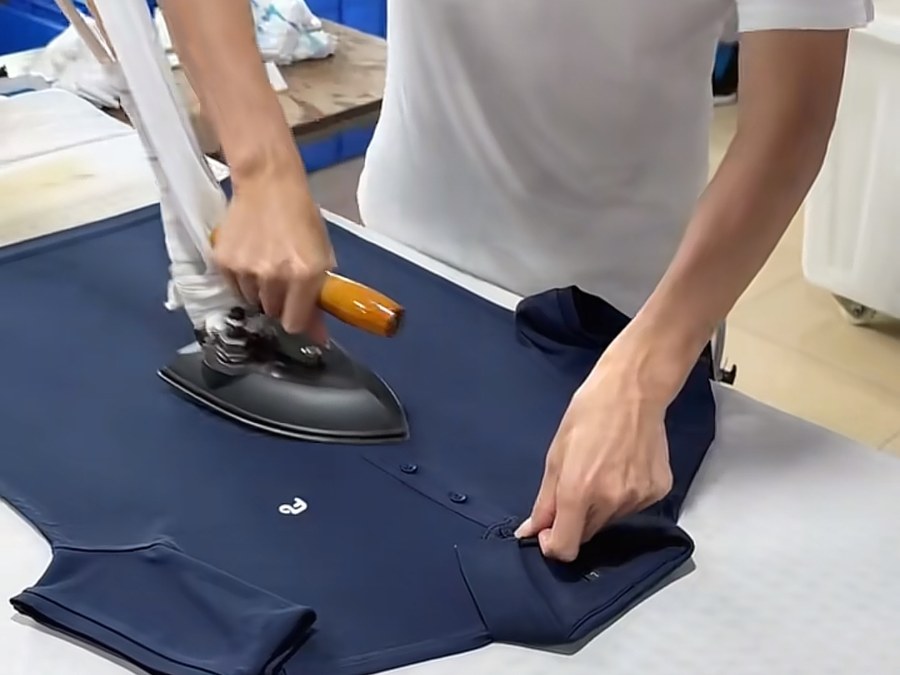 Finisher pressing a navy polo shirt before packing at a hospitality uniform manufacturer