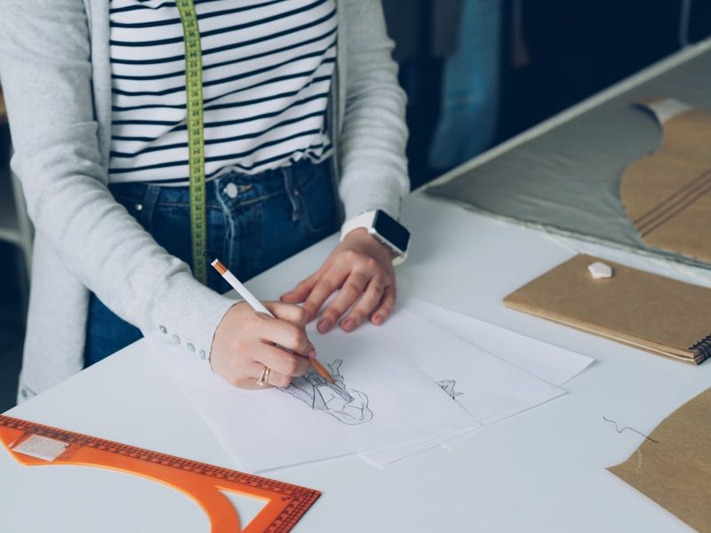Fashion designer sketching a garment design with pattern pieces for ODM clothing manufacturing development