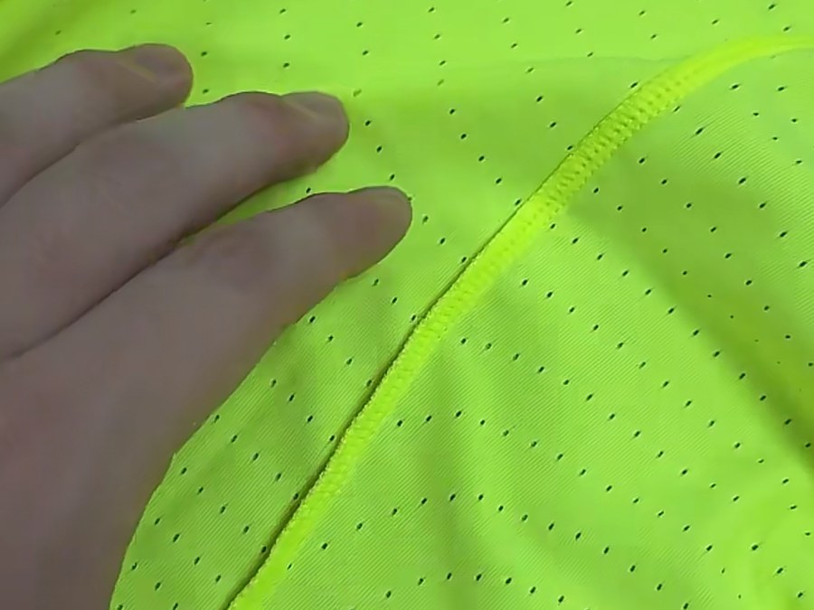 Perforated neon performance fabric with flatlock seam inspected at a sportswear manufacturer