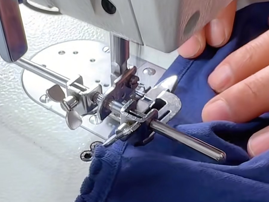 Sewing operator running a navy sample garment through a binding machine at a startup clothing manufacturer