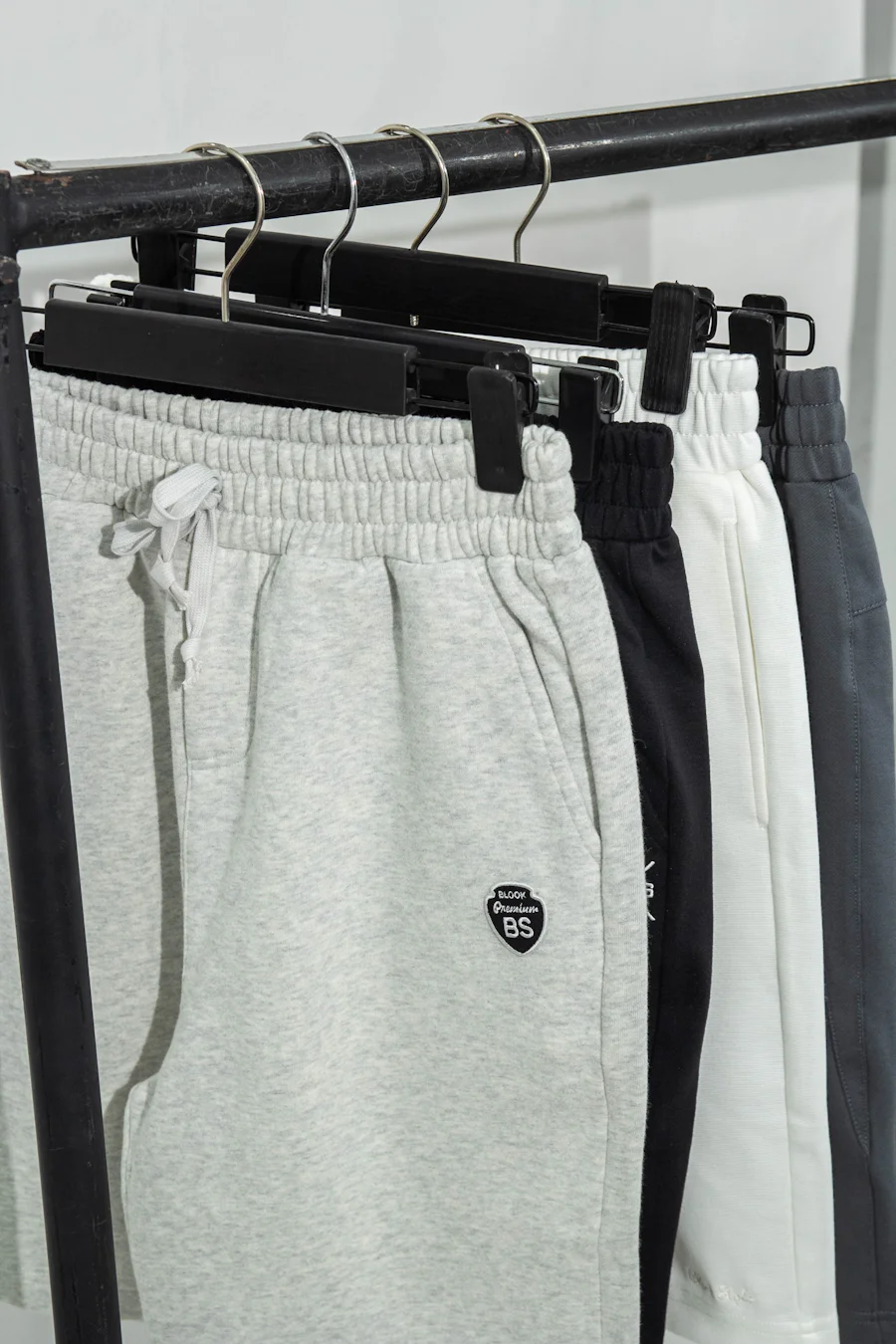 Gray, black, and white sweatpants hanging on a factory rack showing elastic waistband and drawcord construction