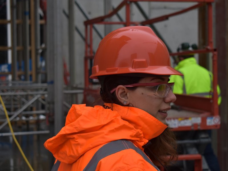Worker wearing an orange hi-vis jacket and hard hat with safety glasses