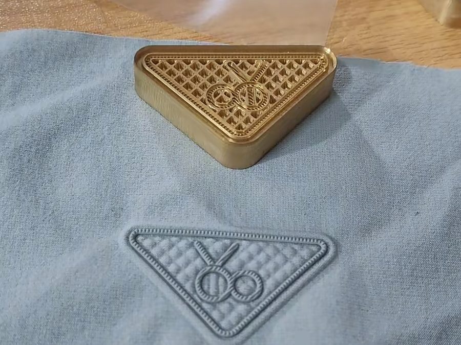 Brass pressing mold next to a finished raised silicone patch on grey fabric