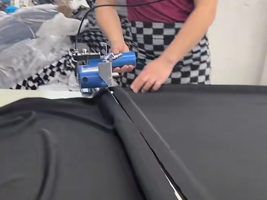 Worker using a handheld electric cutter to trim black fabric on the cutting table