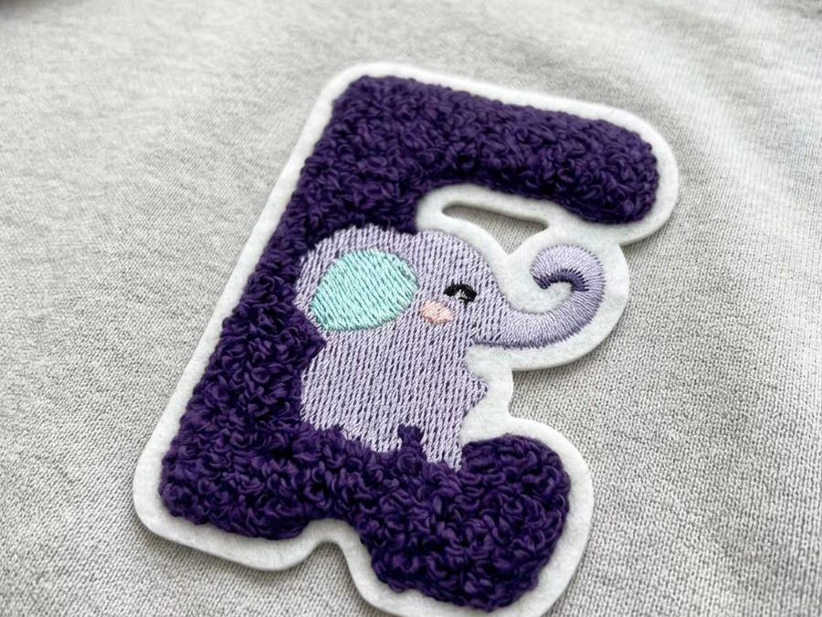 Purple chenille letter patch with an embroidered elephant design on a grey hoodie
