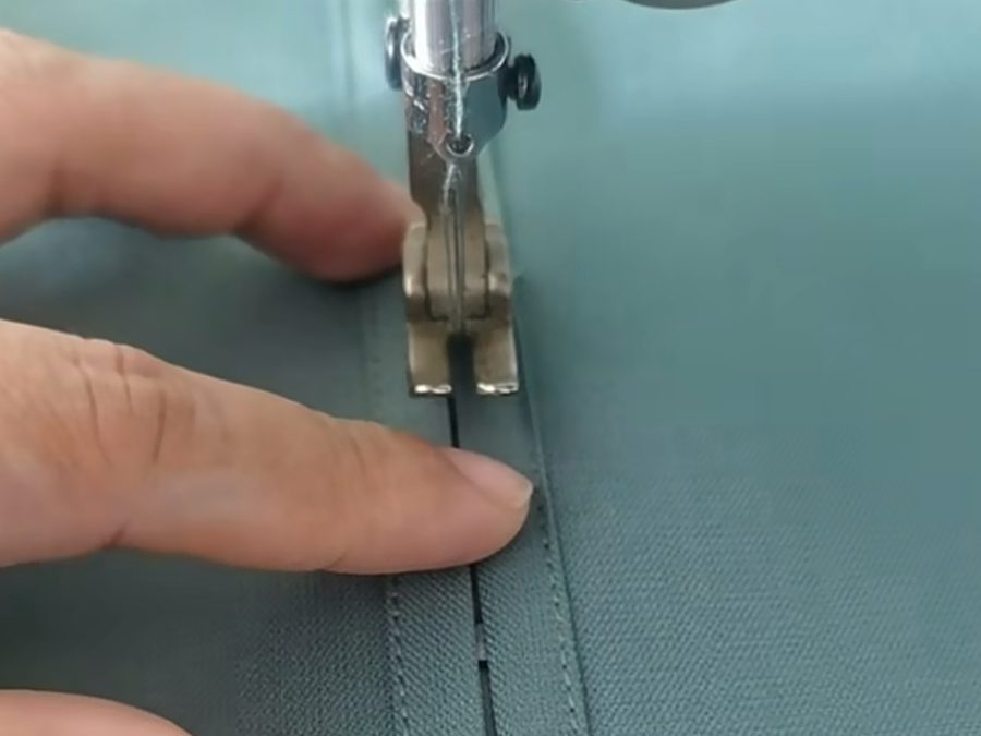 Sewing machine operator hand-guiding a fabric sample during clothing sample development