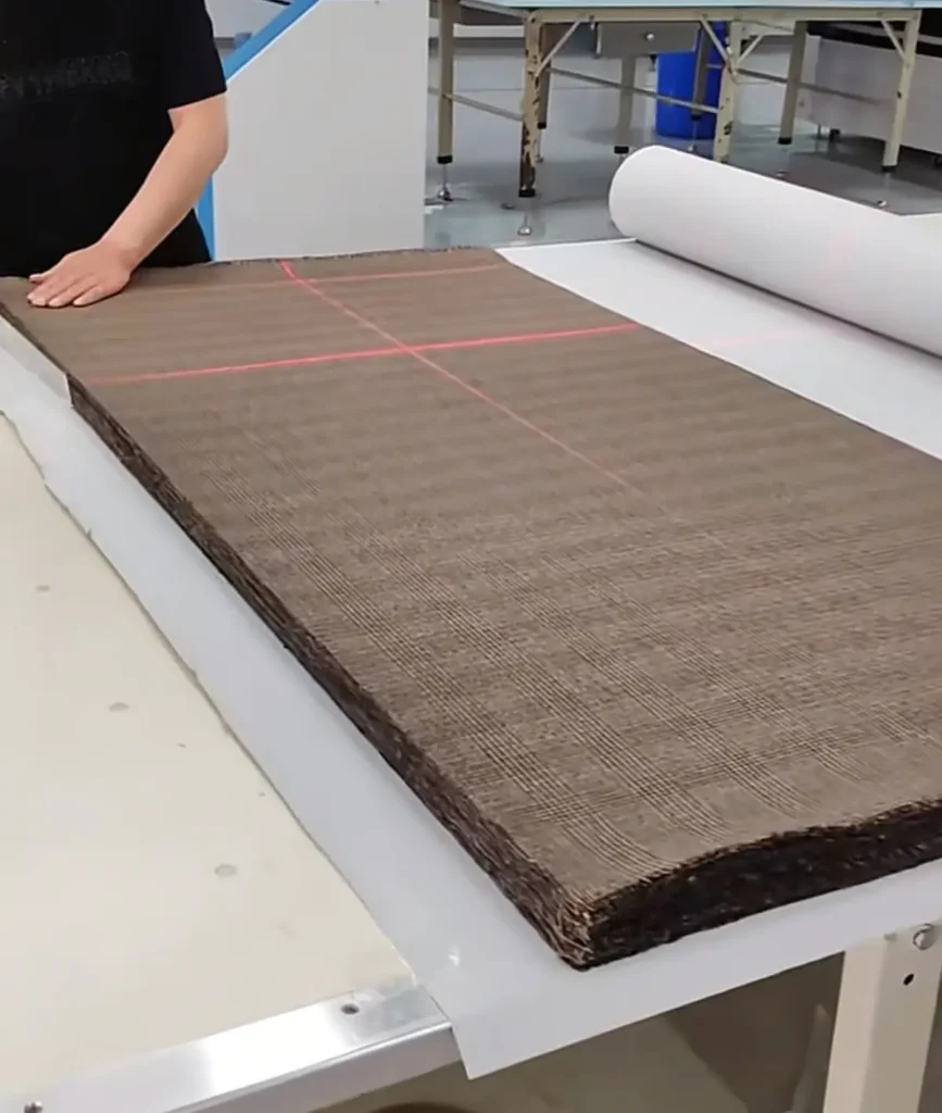 Factory worker inspecting an incoming fabric roll against laser alignment guides before cutting for a clothing manufacturing order