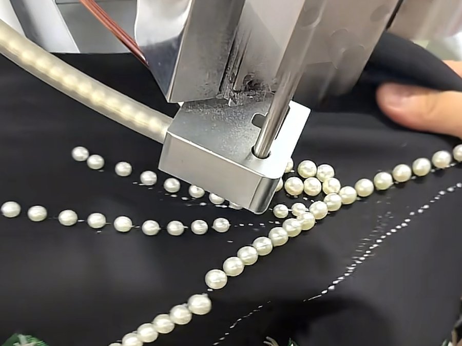 Hand-guided machine setting pearl beading embellishment on black fabric for a fashion brand order