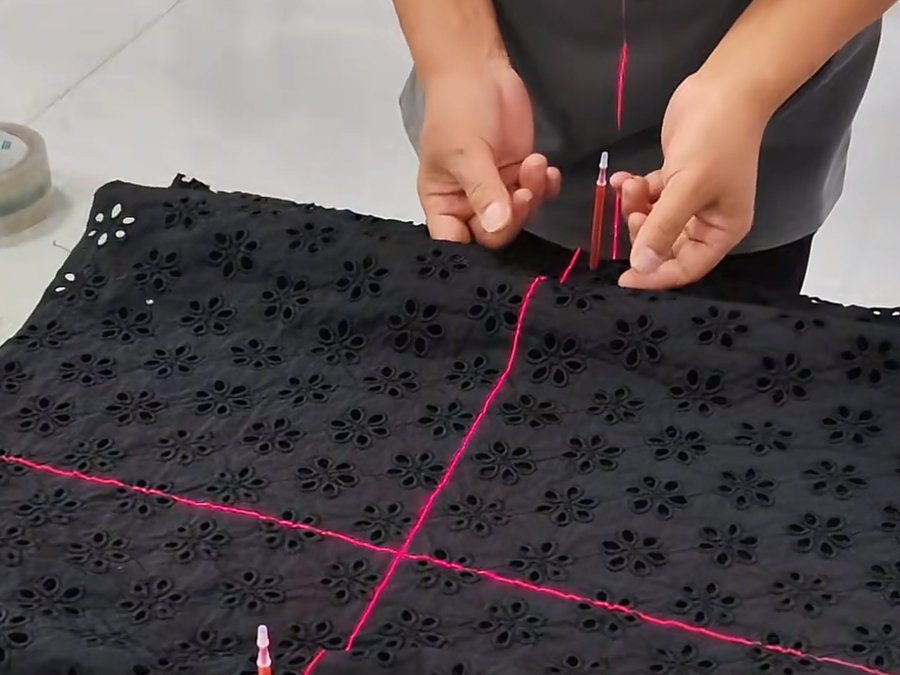 Hands aligning laser-guided cutting lines on eyelet lace fabric to match print placement across a size run