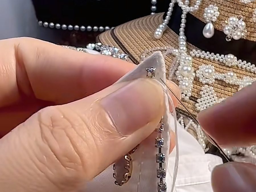 Hand sewing a rhinestone onto white fabric next to pearl and rhinestone beaded appliques