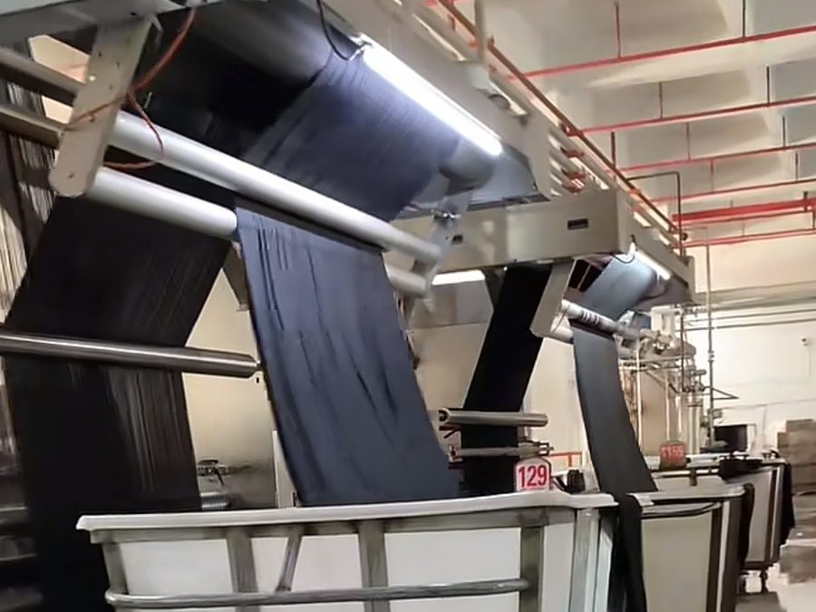Fabric running through a dye vat with batch number tag for color-matched hospitality uniform reorders