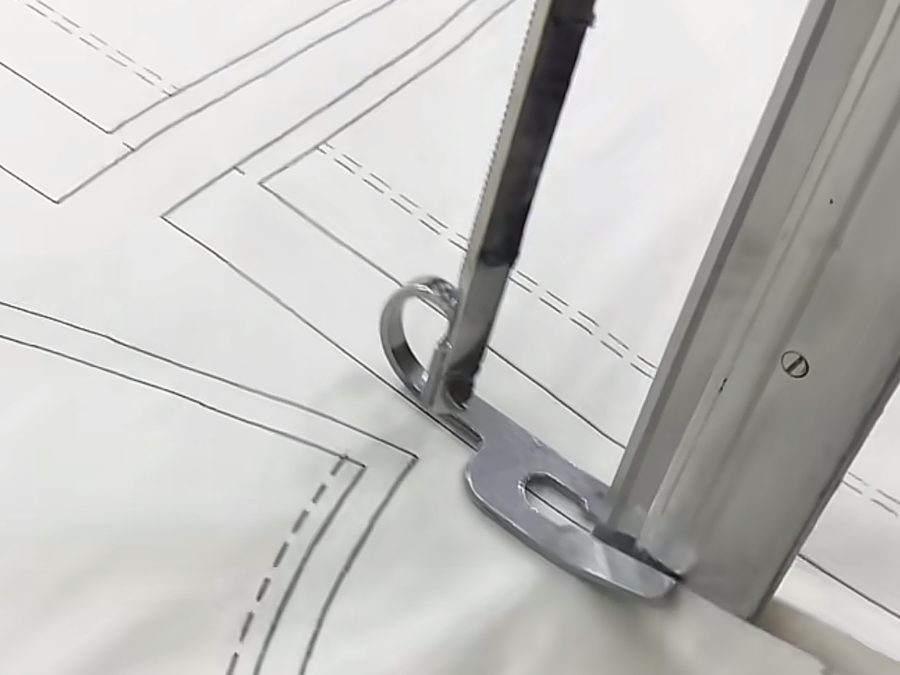 Pattern marking tool tracing a garment pattern during OEM clothing manufacturing feasibility review