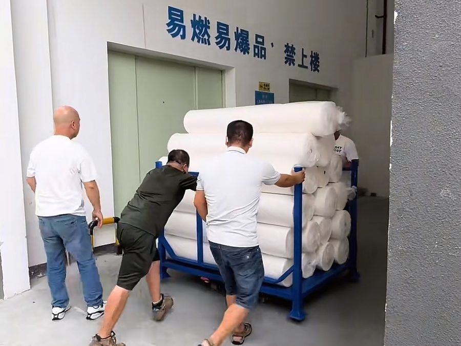 Two factory workers pushing a cart of fabric rolls through a warehouse corridor