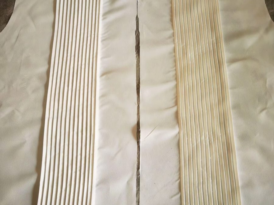 Cream fabric garment panel with knife pleats pressed into vertical sections