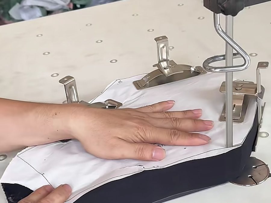 Hand positioning a waistband pattern piece under a sewing machine during school uniform construction