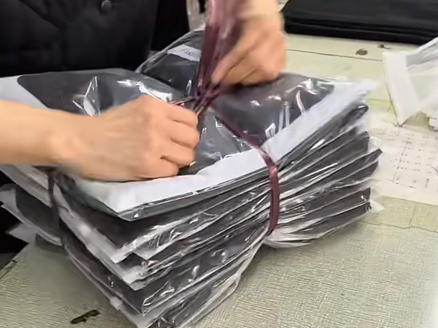Hands bundling and tagging a small stack of finished garments for a startup brand's first shipped order