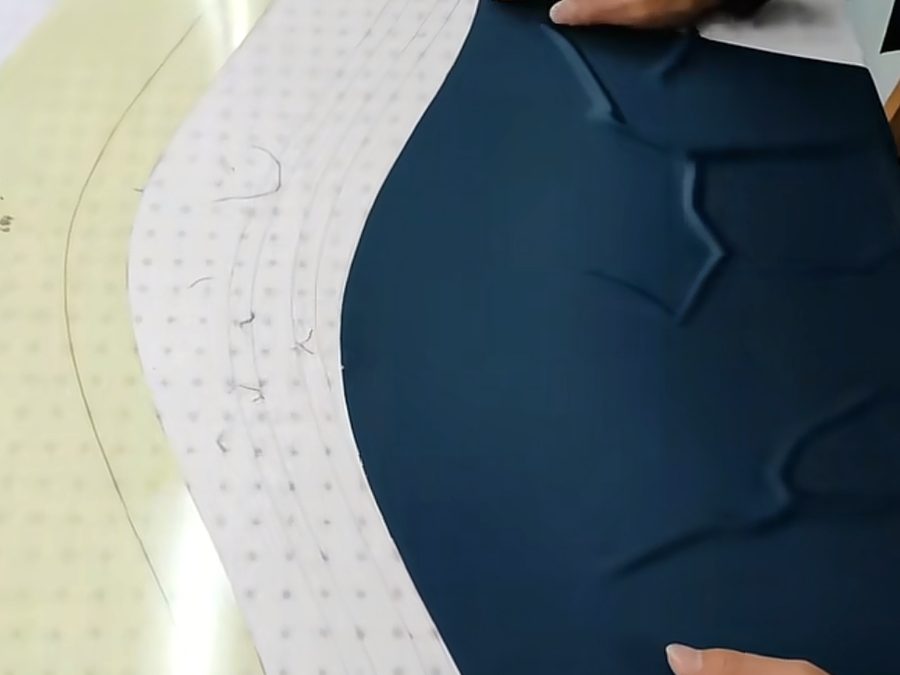 Hands aligning a navy pattern piece against grid dot paper on a cutting table