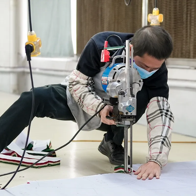Factory worker using an electric round-knife cutter to cut fabric for tee production