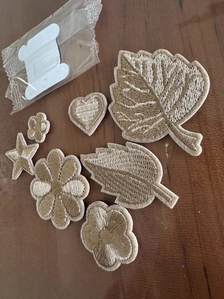 Embroidered appliqué motifs in beige thread — leaves, flowers, a heart and a star — cut to shape and laid on a wood table