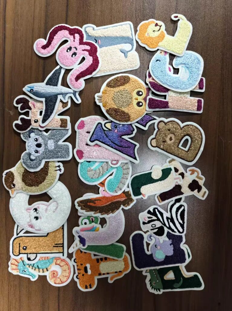 Chenille alphabet letter patches with looped yarn pile and felt backing, laid out on a wood surface