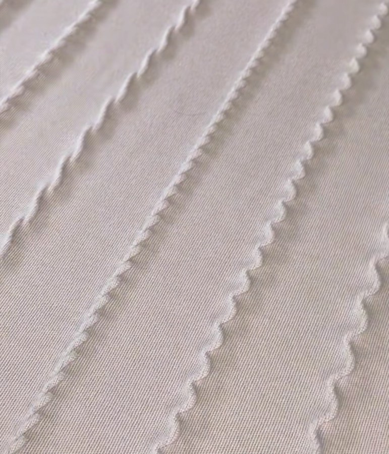 Rows of decorative zig-zag stitching on cream woven fabric, close-up detail of embellishment work