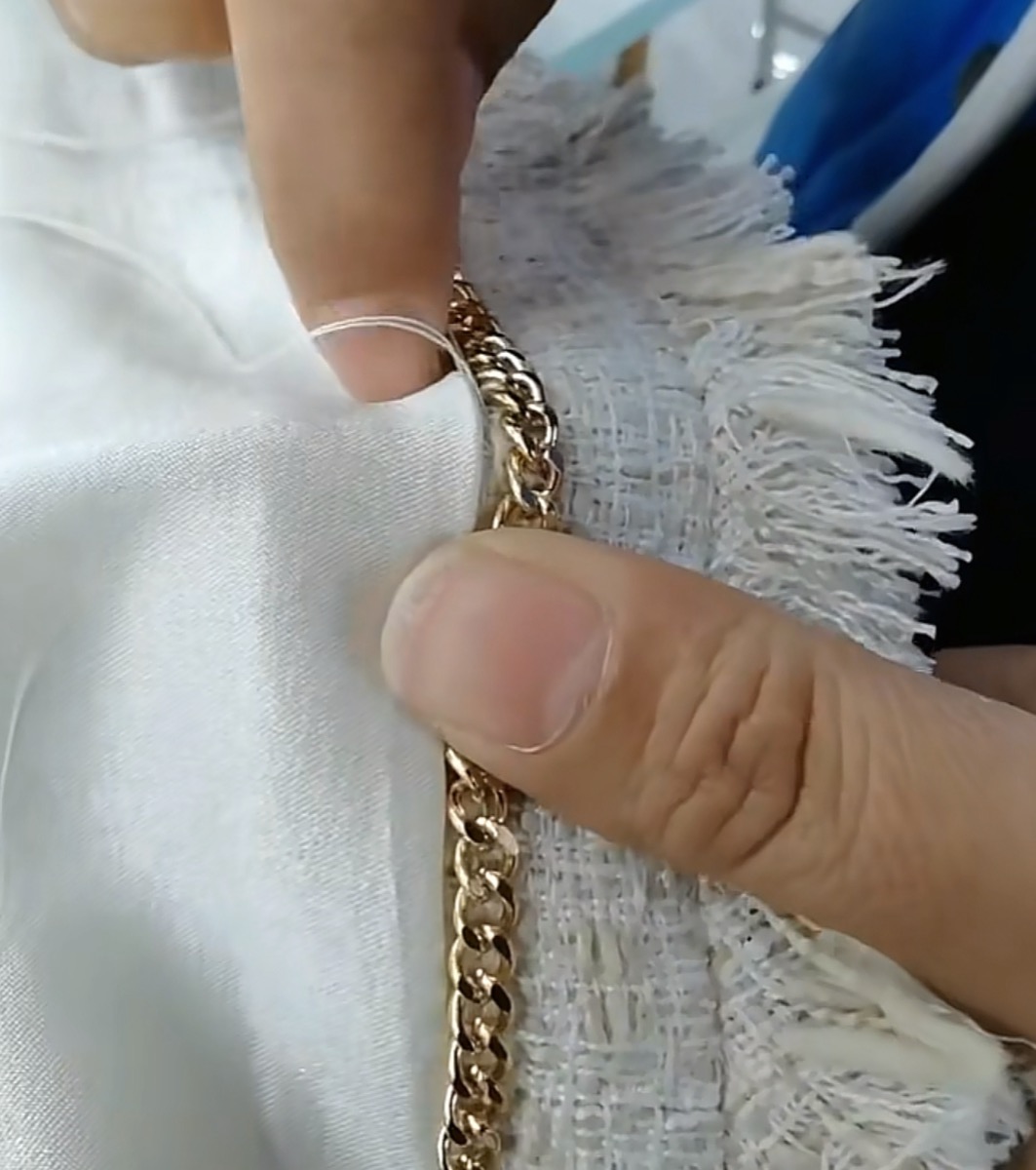 Hands attaching decorative gold chain trim to a white garment panel