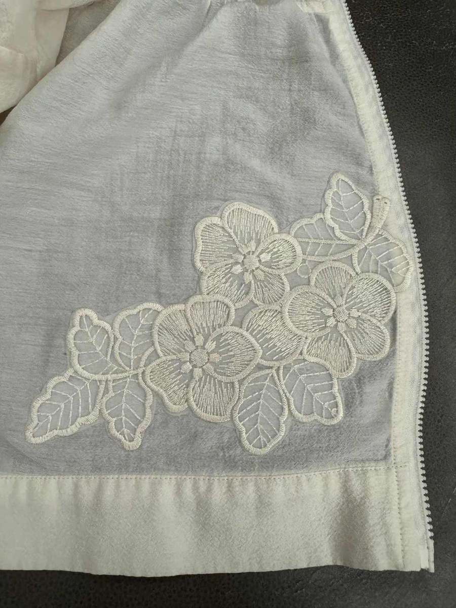 Embroidered floral appliqué on white fabric garment, close-up showing satin-stitch flower and leaf motifs