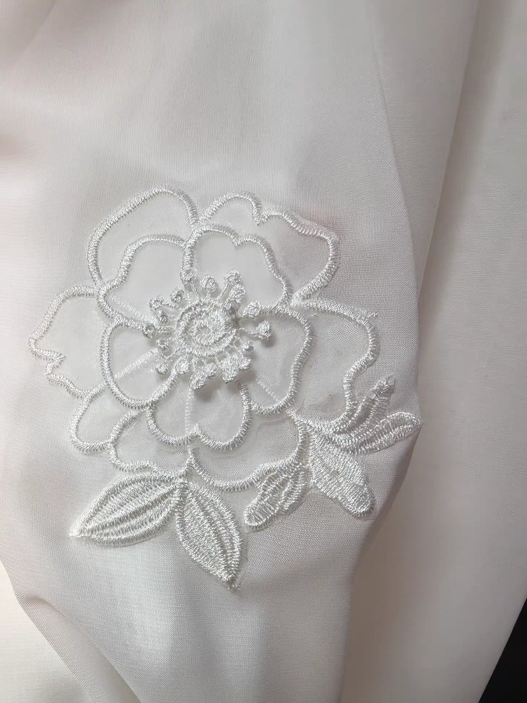 A white embroidered floral motif stitched onto lightweight white woven fabric