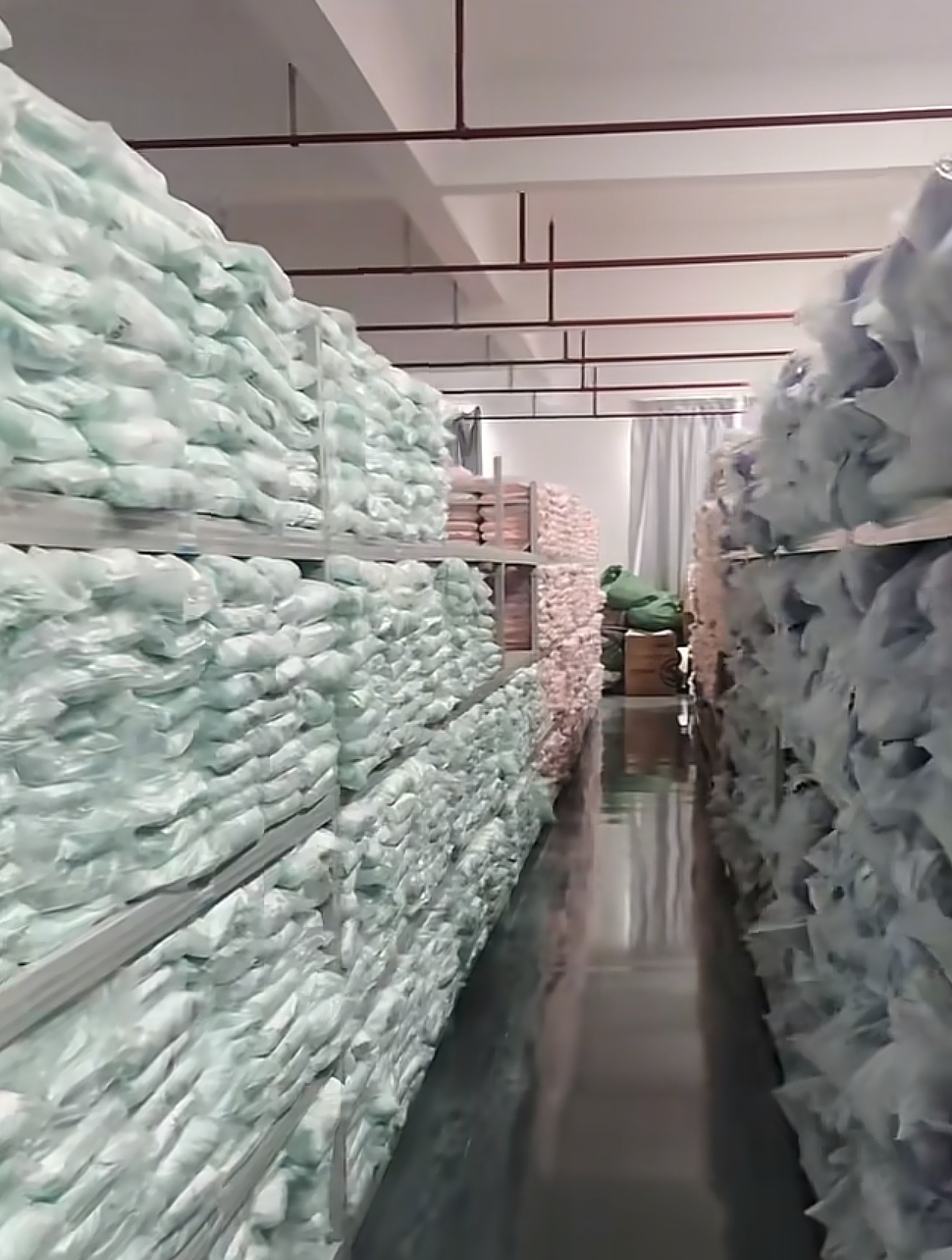 Rolled fabric bolts sorted by color on warehouse shelving ahead of a cutting or pleating order