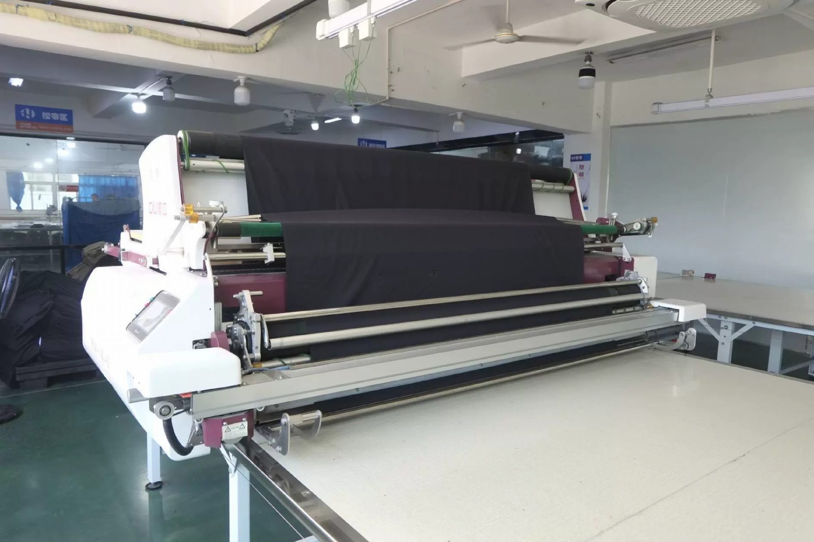 Fabric spreading machine feeding folded dark fabric onto a cutting table