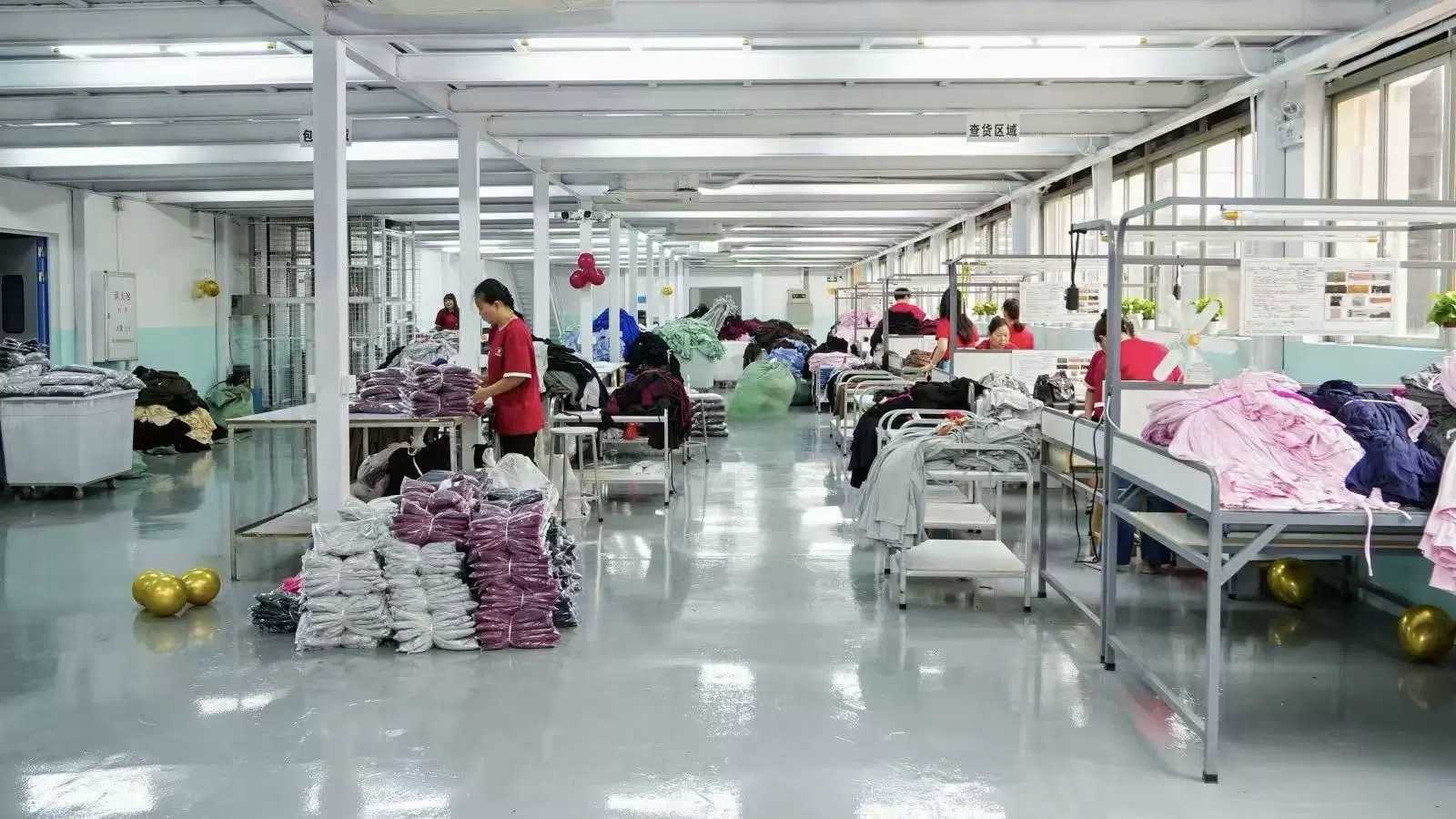 Workers checking and folding finished garments at inspection tables, with bagged stacks on the floor