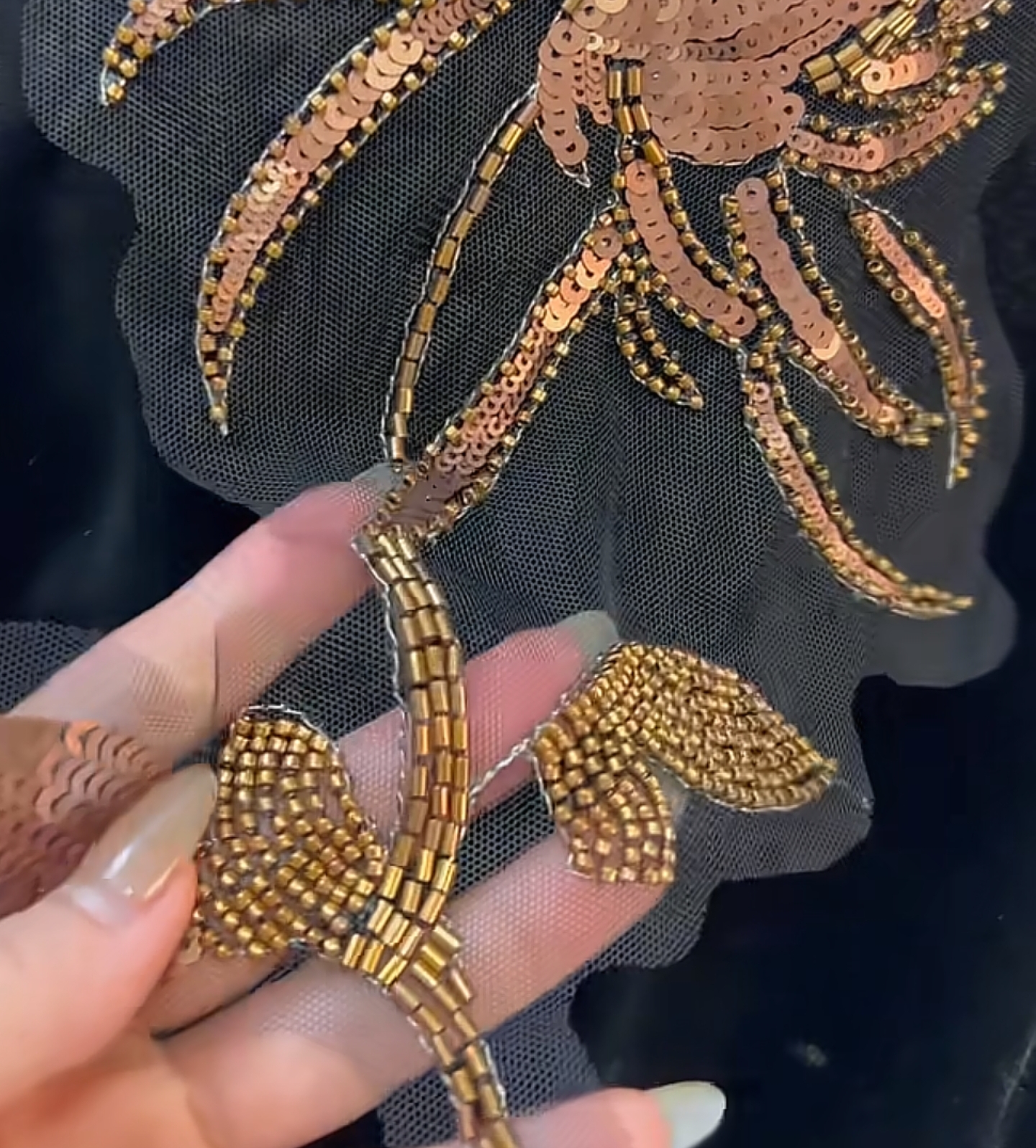 Gold sequin and bead floral motif embroidered onto black tulle, held up for inspection