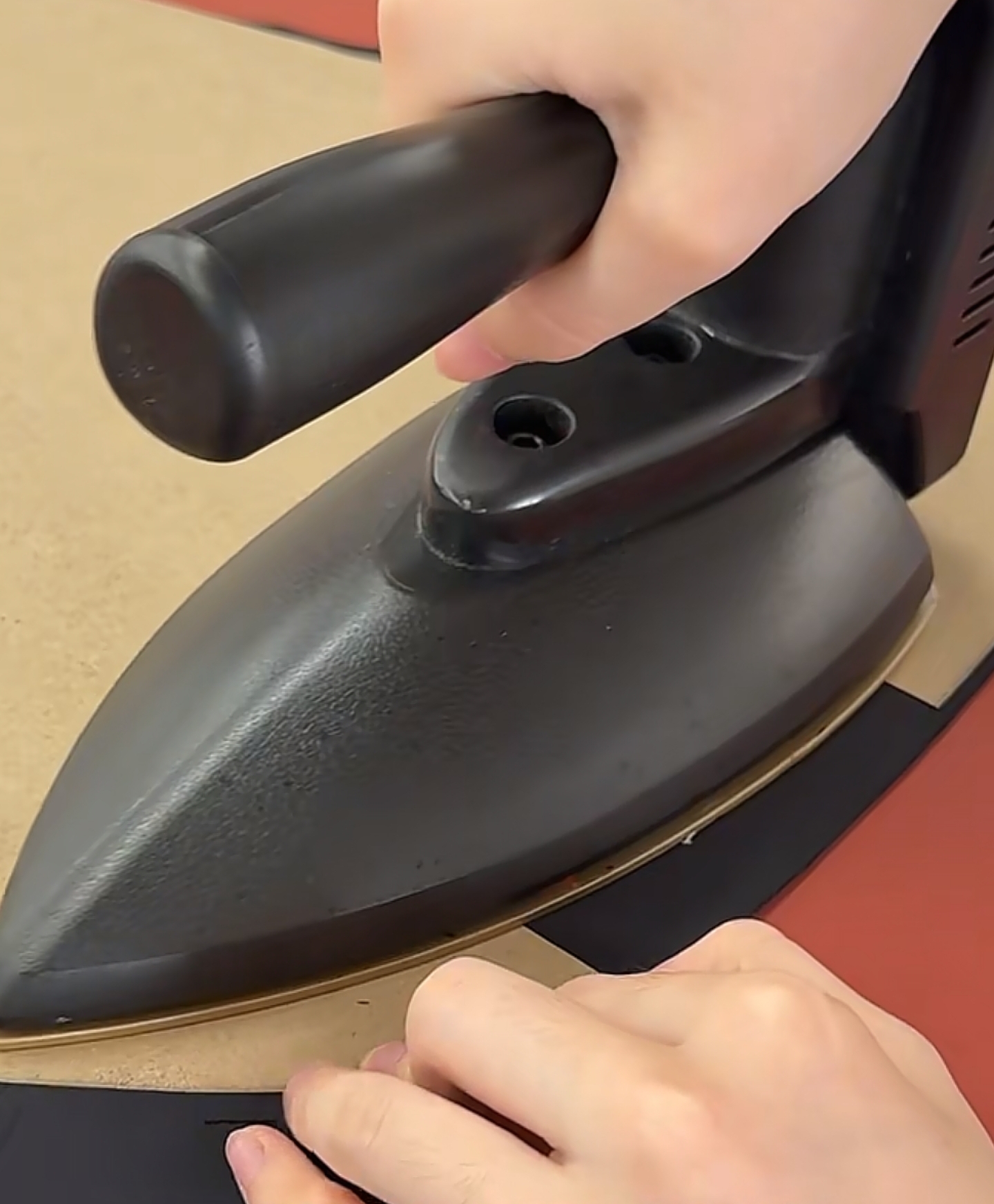 Hand iron being pressed onto dark fabric on a pressing table