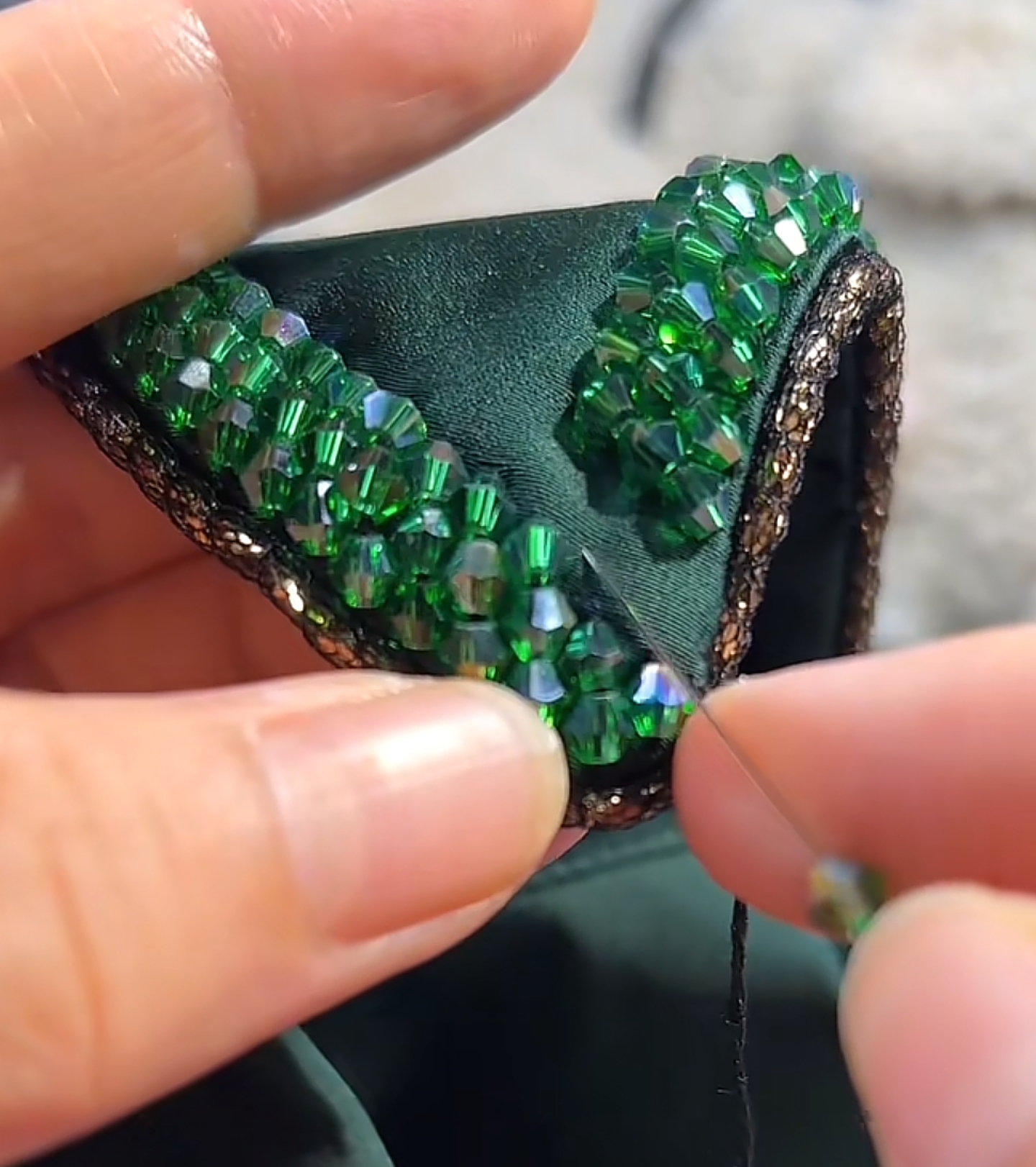 Hand sewing green faceted crystal beads onto fabric with a needle and thread, close up