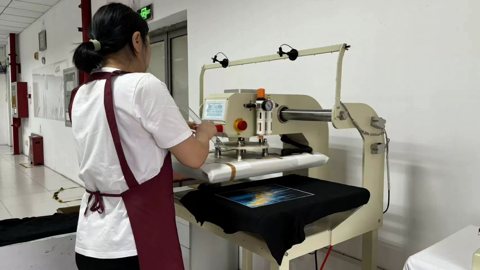 Operator at a pneumatic heat press with a printed transfer laid on a black T-shirt