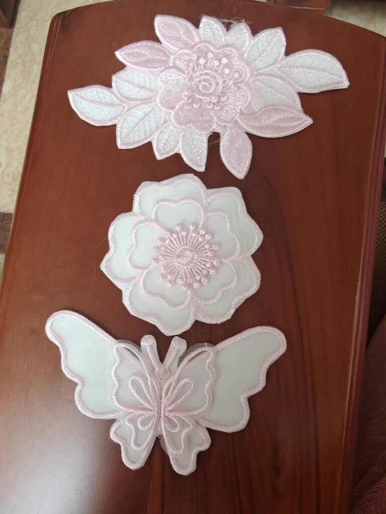 Layered pink and white flower and butterfly appliqué pieces with beaded centres, on a wood table