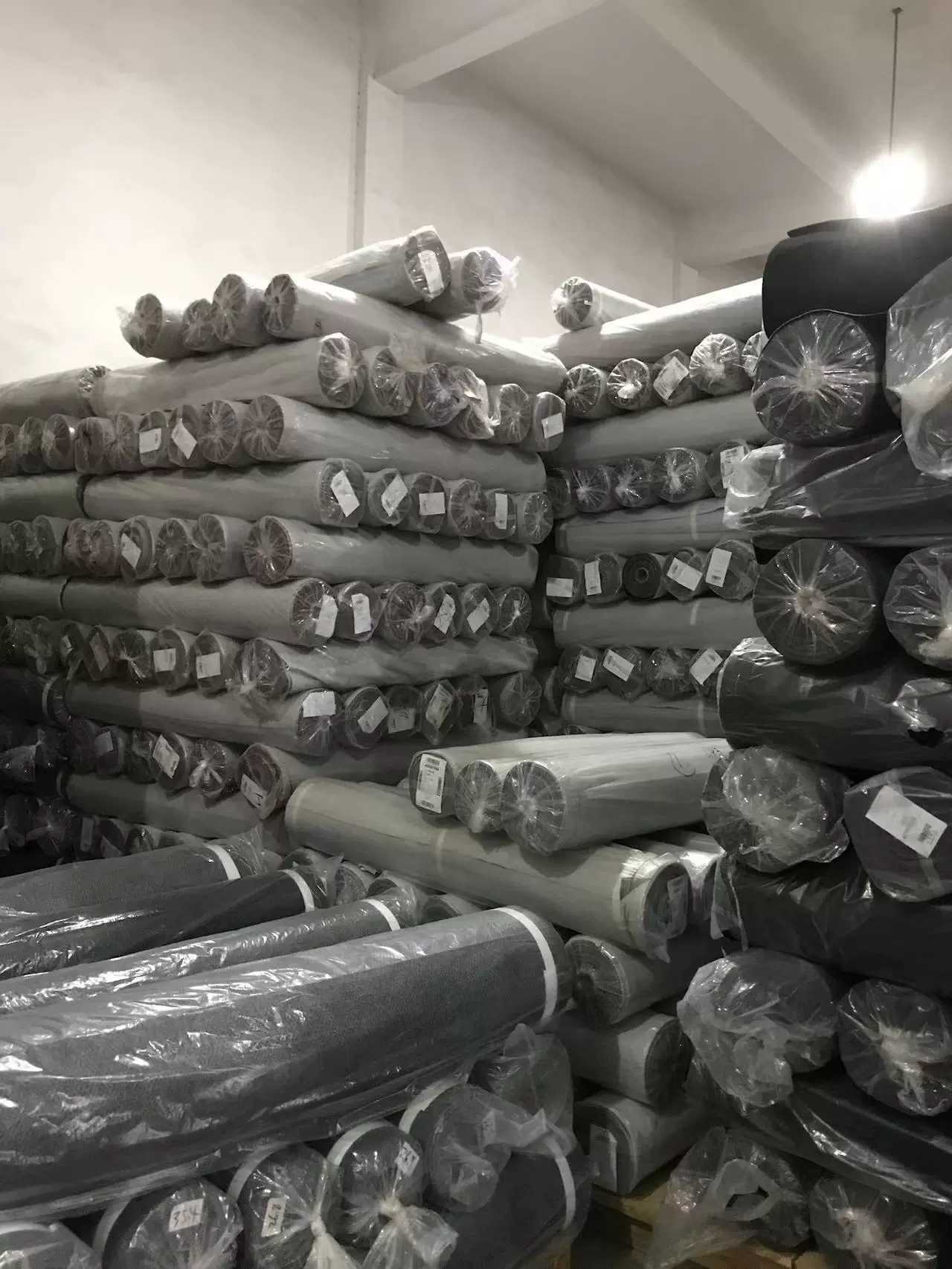 Stacked rolls of grey fabric wrapped in plastic in a garment factory fabric warehouse