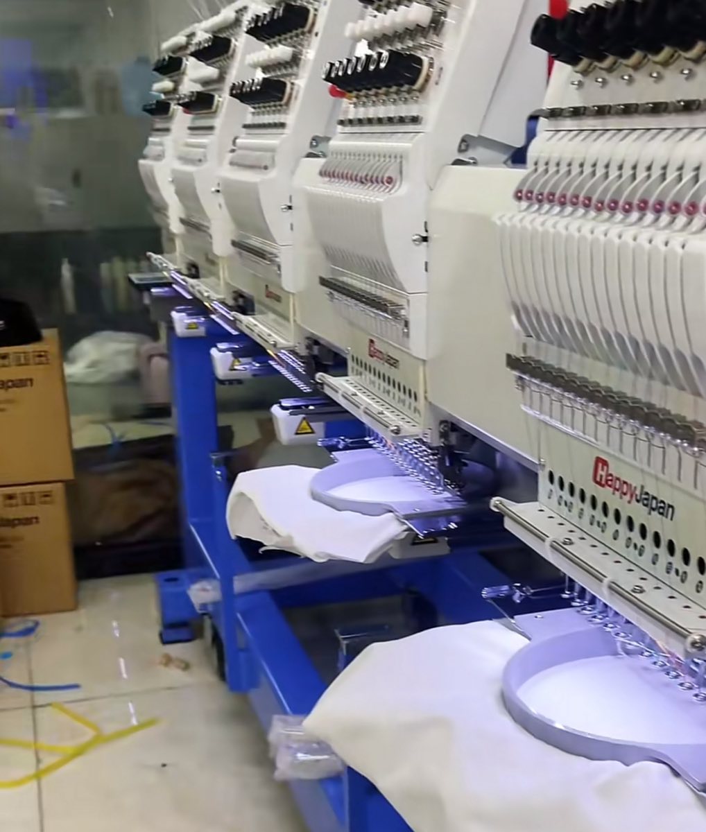 Row of HappyJapan multi-head embroidery machines with white garments hooped and ready for production on our factory floor