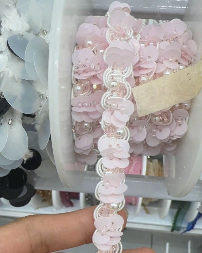 A reel of pale pink sequin trim with small pink beads, one length held between two fingers