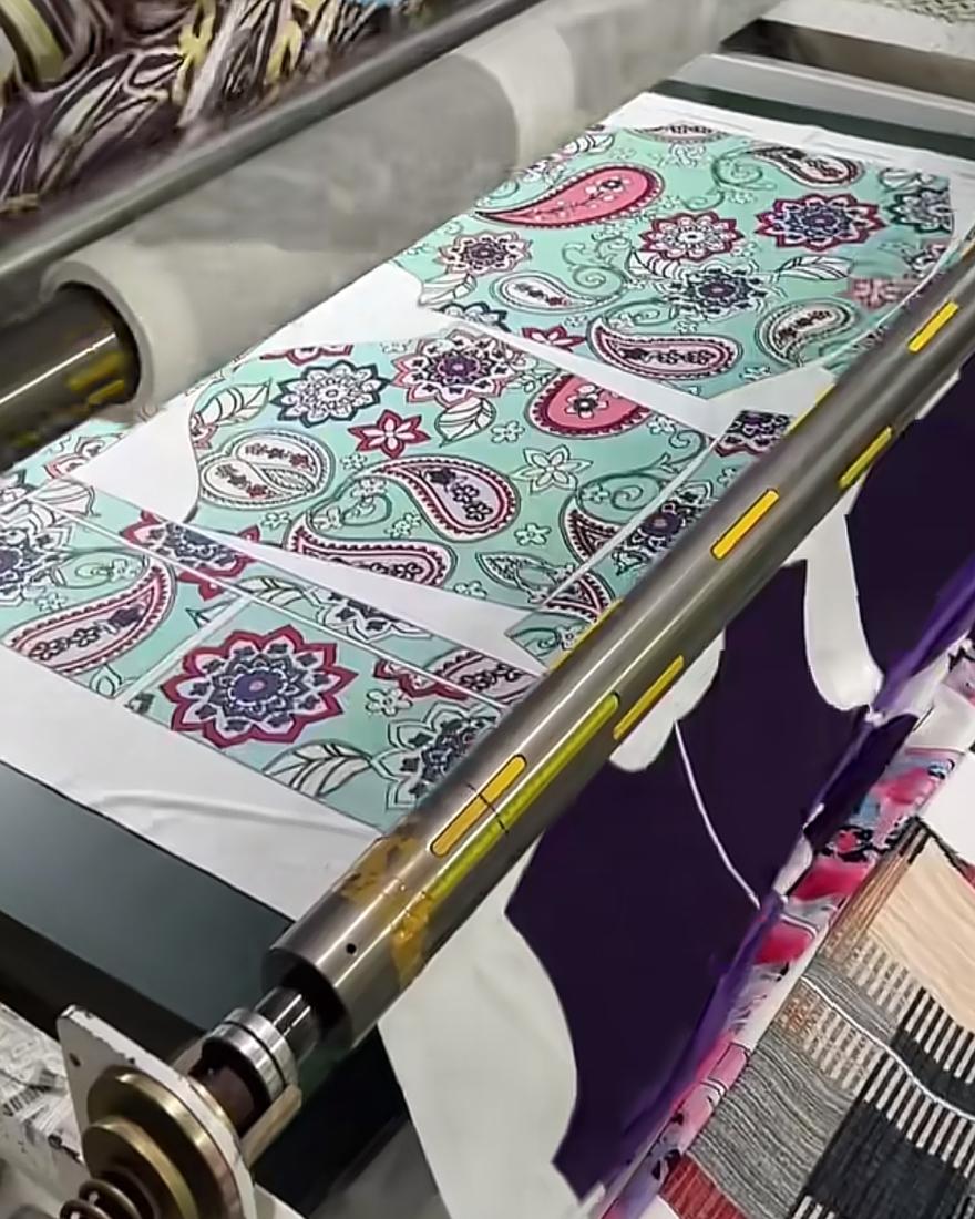 Cut garment panels in a turquoise paisley print passing under the roller of a heat transfer calender